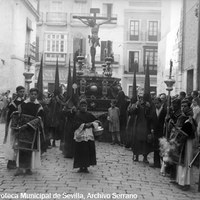 8. JUAN JOSÉ SERRANO GÓMEZ. Crucificado del Calvario. 1928-1930.  Se nos presenta en una estampa irrepetible. La imagen de Francisco de Ocampo, discípulo de Martínez Montañés, ha girado en la esquina de la antigua calle Magdalena y se encamina por la actual calle Cristo del Calvario, por la que entonces hacía la entrada al templo. A la derecha, la capilla de la Virgen de la Antigua y Siete Dolores, actual iglesia de la Hermandad de Montserrat. © ICAS-SAHP, Fototeca Municipal de Sevilla, Archivo Serrano