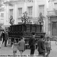 15. RAFAEL CUBILES LÓPEZ. Traslado a su capilla del nuevo paso de la Virgen de la Soledad de San Buenaventura por la plaza del Duque. 1957 Una imagen habitual en las calles de Sevilla en los días previos a la Semana Santa.  Y como testigo mudo, el palacio de Cavalieri, derribado en 1963 para la construcción de los antiguos almacenes Lubre, de los que sólo se conserva la portada, procedente del palacio de Quirós de la plaza de la Gavidia.  © ICAS-SAHP, Fototeca Municipal de Sevilla, Archivo Cubiles