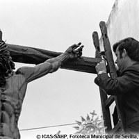 19. RAFAEL CUBILES LÓPEZ. Un hermano recompone la fractura de un dedo del Cristo de la Sangre. 1969 El crucificado, tallado por Francisco Buiza, realizó su primera estación de penitencia en 1967. A consecuencia de la salida de la iglesia, la imagen del segundo paso de la Hermandad de San Benito sufrió una rotura que fue reparada al instante y en plena calle. © ICAS-SAHP, Fototeca Municipal de Sevilla, Archivo Cubiles